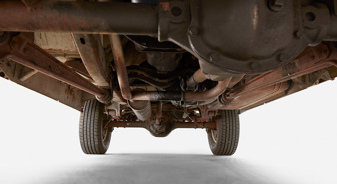 View of vehicle underside focusing on suspension components, axle, and tire with rust present