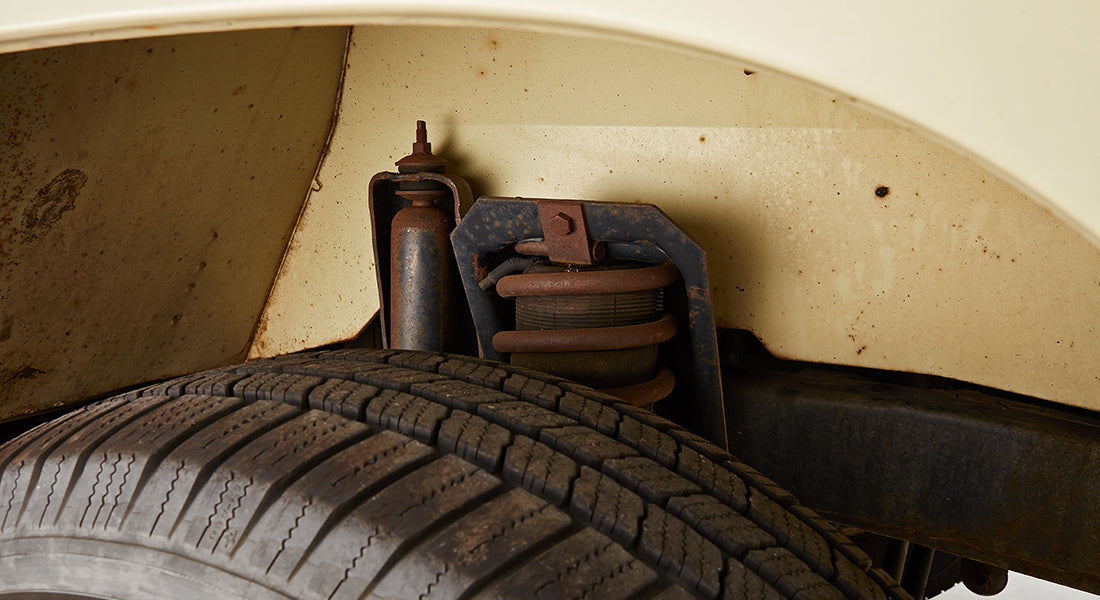Underbody view of a vehicle showing exhaust pipes, axles, and tires on a clean white surface