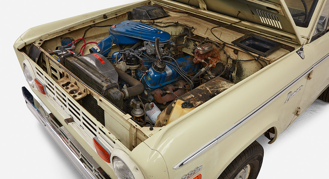Classic Ford Bronco front corner with engine bay view including blue valve covers and battery
