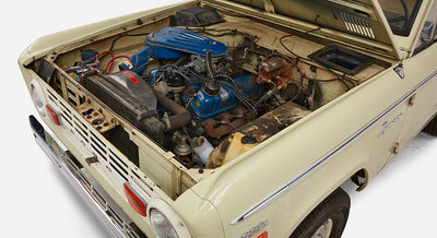 Classic Ford Bronco front corner with engine bay view including blue valve covers and battery