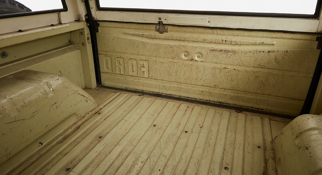 Interior cargo area of Classic Ford Bronco showing empty dirty beige bed with FORD emboss