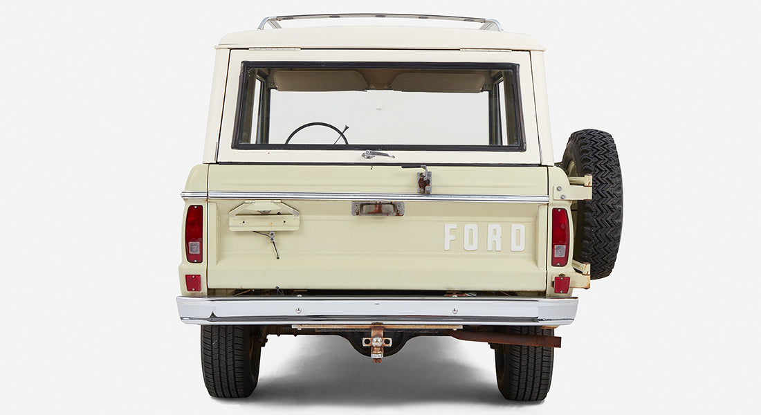 Rear view of light sage green Classic Ford Bronco with white roof and spare tire mounted on back