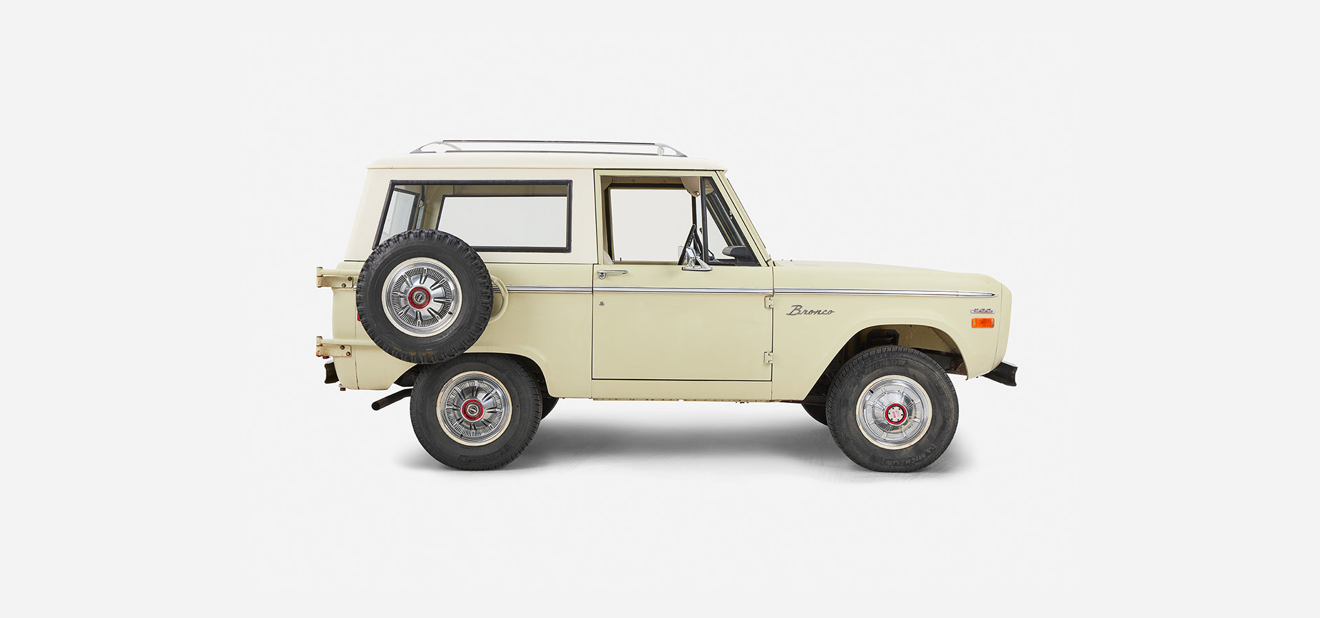Side profile of a light yellow Classic Ford Bronco with white roof and spare tire mounted on rear