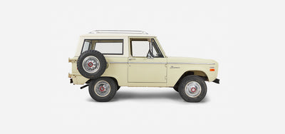 Side profile of a light yellow Classic Ford Bronco with white roof and spare tire mounted on rear