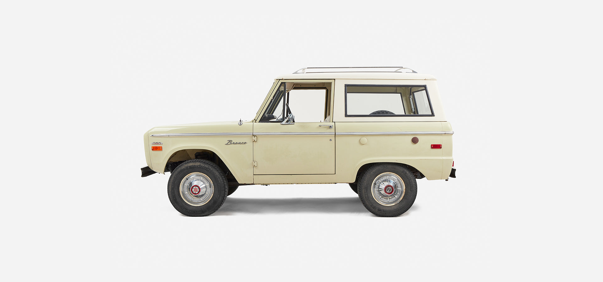 Side profile of a light yellow Classic Ford Bronco with white roof against plain background