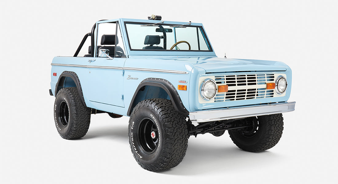 Front three-quarter close-up of a baby blue Classic Ford Bronco with black trim and off-road tires