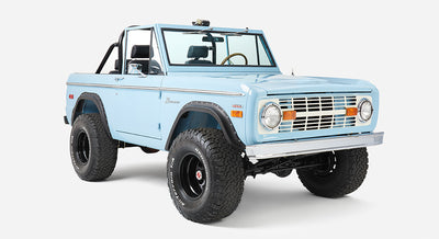 Front three-quarter close-up of a baby blue Classic Ford Bronco with black trim and off-road tires