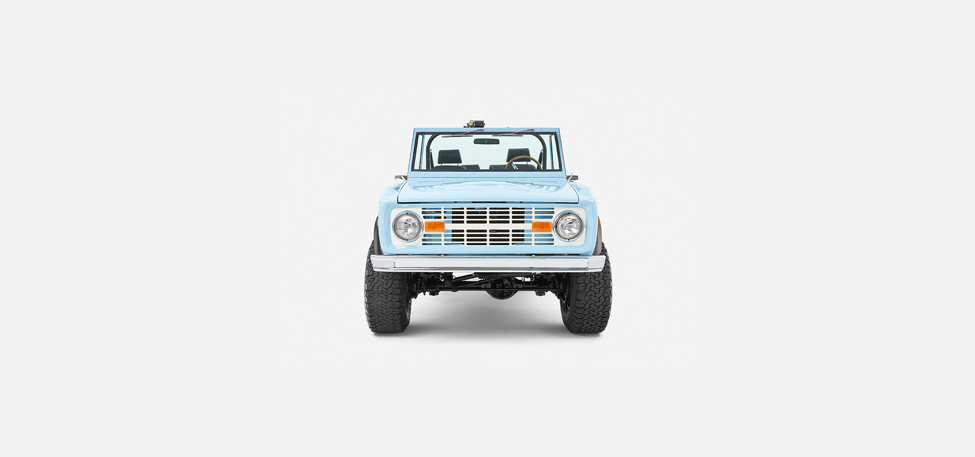 Front view of a baby blue Classic Ford Bronco with round headlights and orange signals