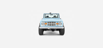 Front view of a baby blue Classic Ford Bronco with round headlights and orange signals