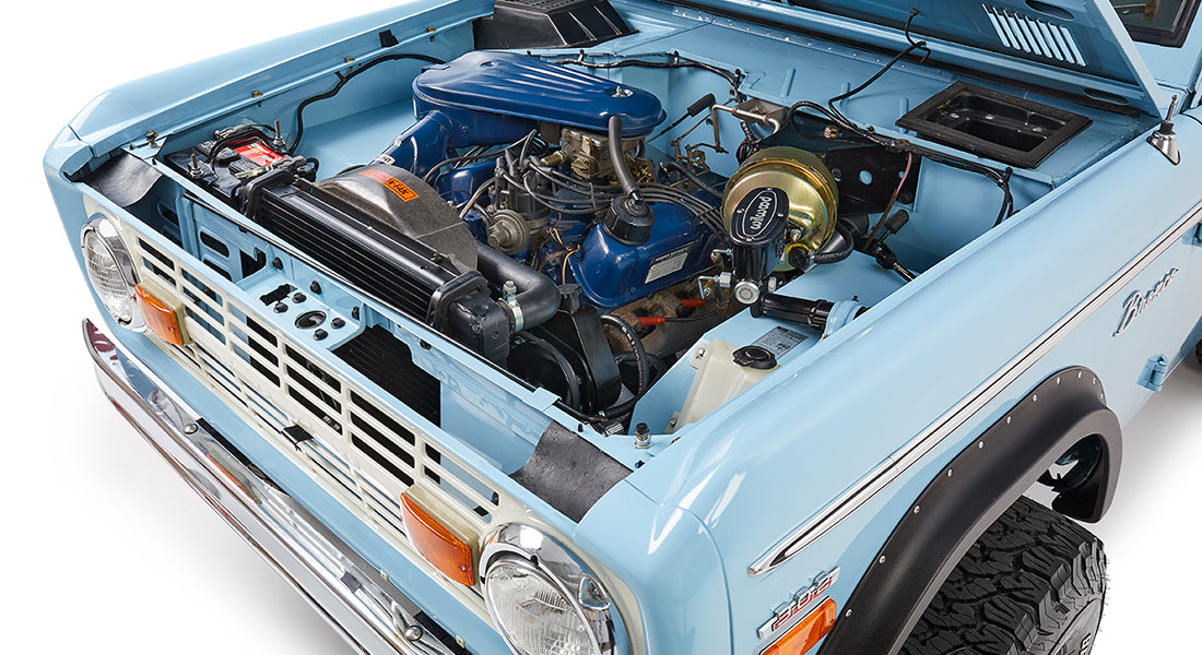 Open hood displaying clean engine compartment of baby blue Classic Ford Bronco