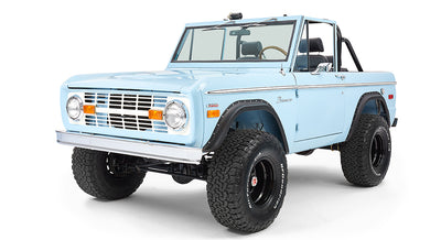 Side front view of light blue Classic Ford Bronco with black wheels and raised suspension on white background