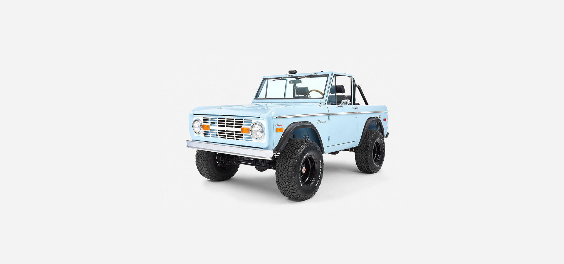 Front three-quarter view of baby blue Classic Ford Bronco with roll cage and black wheels