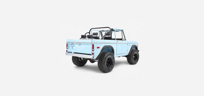 Rear three-quarter view of baby blue Classic Ford Bronco with open top and roll cage