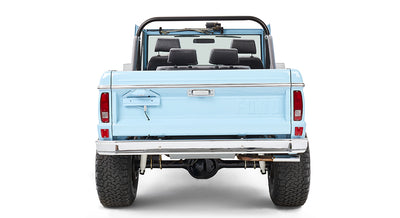 Rear view of light blue Classic Ford Bronco with black roll bar and open tailgate on white background
