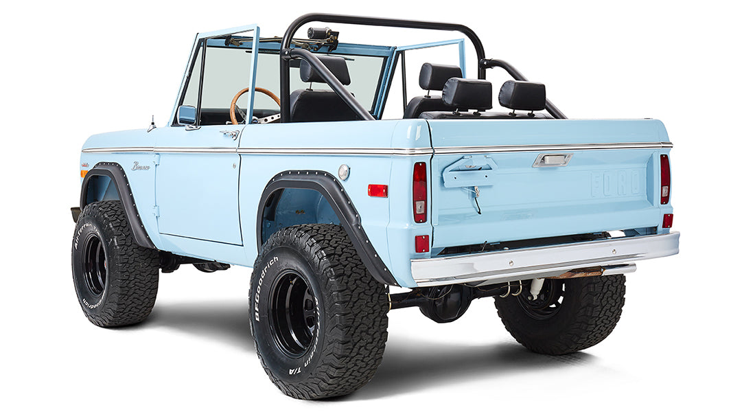 Classic Ford Bronco in baby blue, rear three-quarter view with large tires and open top.