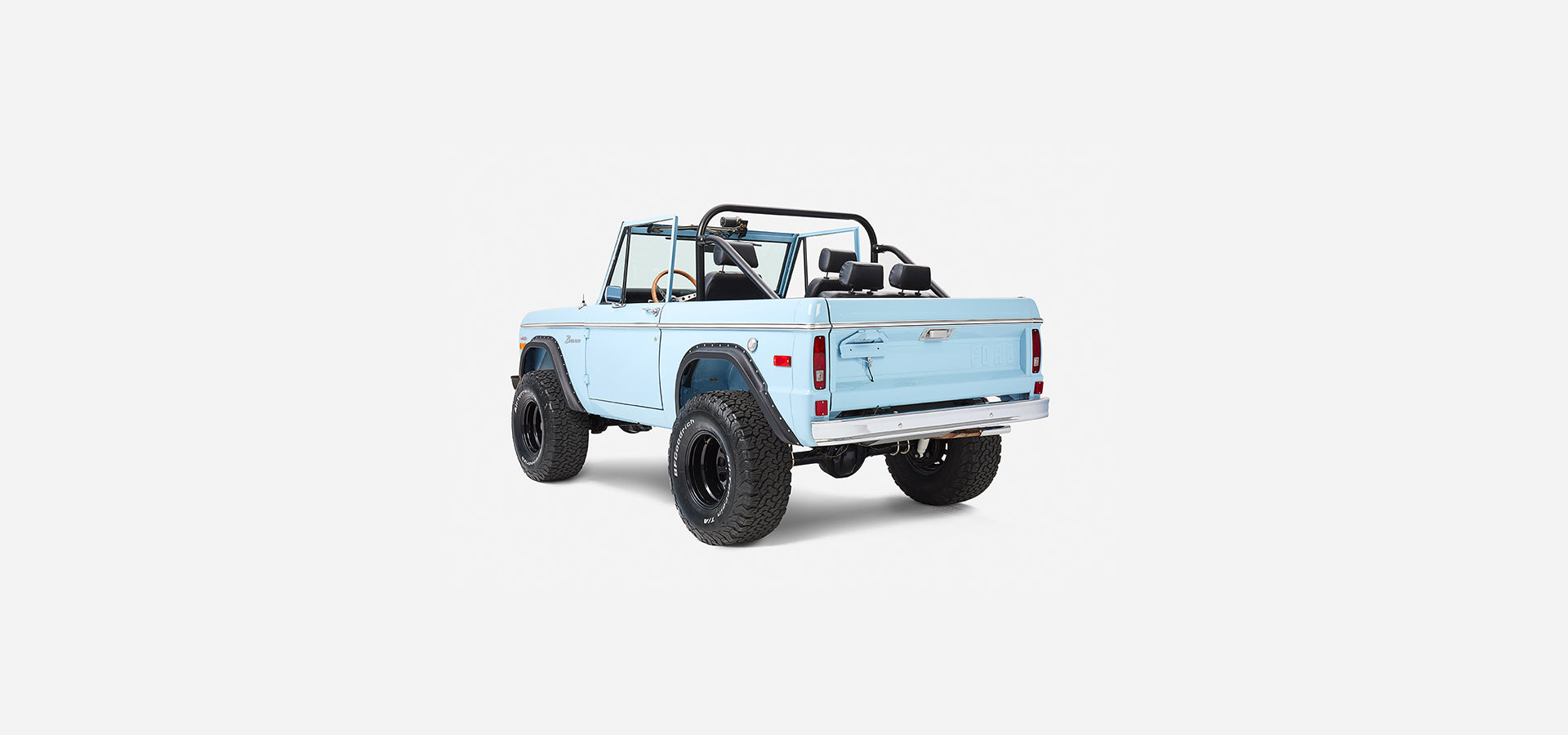 Rear three-quarter view of a baby blue Classic Ford Bronco with black wheels and off-road tires