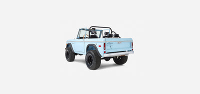 Rear three-quarter view of a baby blue Classic Ford Bronco with black wheels and off-road tires