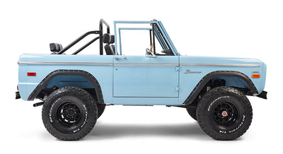 Classic Ford Bronco in baby blue with driver-side door visible, off-road tires, and roll bar.