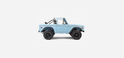 Side profile of a baby blue Classic Ford Bronco with roll cage and black BFGoodrich tires