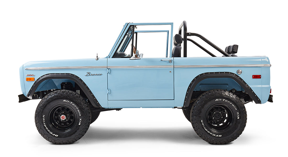 Classic Ford Bronco in baby blue shown in side profile with black fender flares and off-road tires.