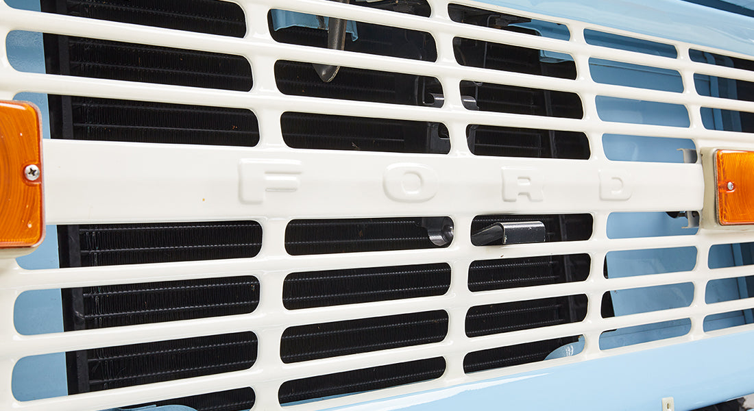 Close-up of the white front grille with FORD lettering on a baby blue classic Ford Bronco.
