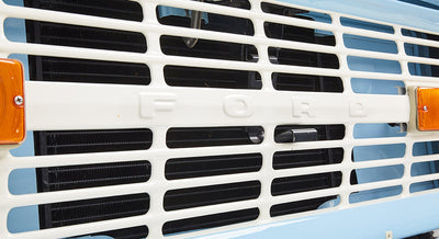 Close-up of the white front grille with FORD lettering on a baby blue classic Ford Bronco.