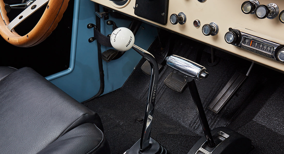Close-up of manual gear shifter with a white Hurst shift knob inside a classic Ford Bronco.