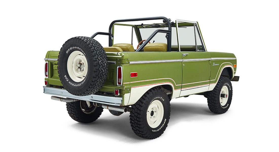 Rear three-quarter view of a green Classic Ford Bronco with white wheels and off-road tires