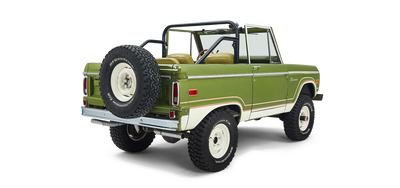 Three-quarter rear view of a green and white Classic Ford Bronco showing spare tire and roll bar.