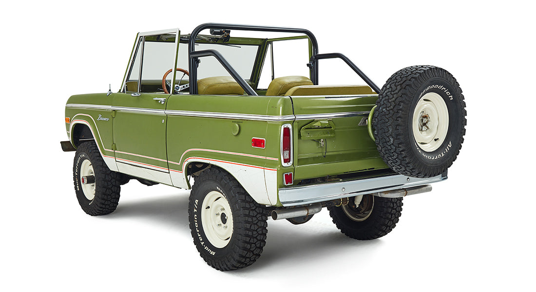 Three-quarter rear view of a green and white Classic Ford Bronco with off-road tires and no roof.