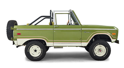 Side profile of a green Classic Ford Bronco with roll cage, white wheels, and off-road tires