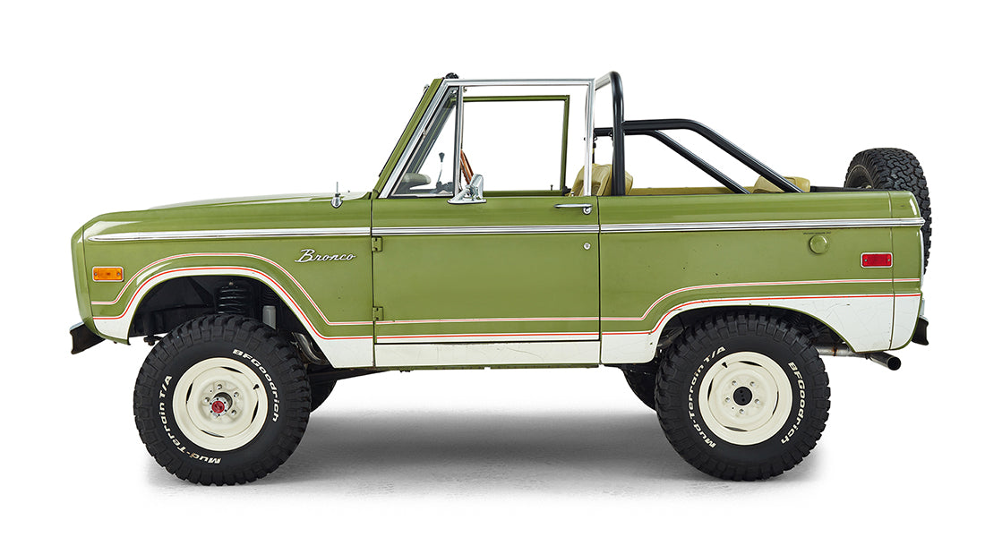 Side view of a green Classic Ford Bronco with white wheels and off-road tires