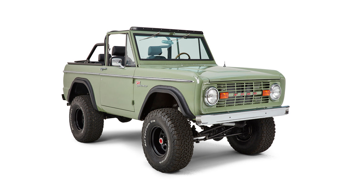 Three-quarter front view of Classic Ford Bronco showing green body, black wheels, and off-road tires