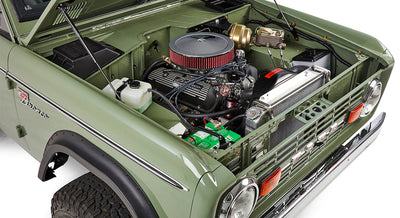 Close-up of engine bay in green Classic Ford Bronco including battery, hoses, and air cleaner.