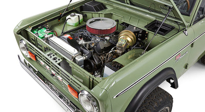 Under-hood view showing engine components and battery inside green Classic Ford Bronco.