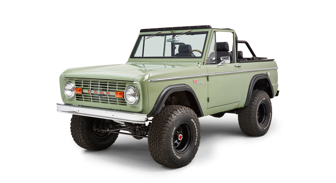 Three-quarter front view of green Classic Ford Bronco showing tires, headlights, and grille lettering.
