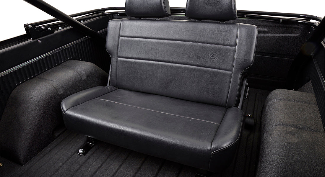 Black leather rear bench seat inside Classic Ford Bronco with textured floor and roll cage visible.