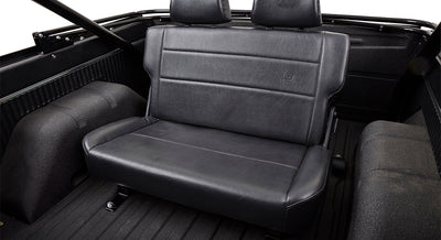 Black leather rear bench seat inside Classic Ford Bronco with textured floor and roll cage visible.