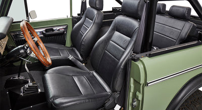Close-up of black leather front seats inside Classic Ford Bronco with wooden steering wheel.