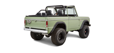 Rear-side view of a green Classic Ford Bronco with black roll cage and off-road tires