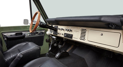 Interior view of Classic Ford Bronco showing wooden steering wheel, black seats and dashboard with controls.