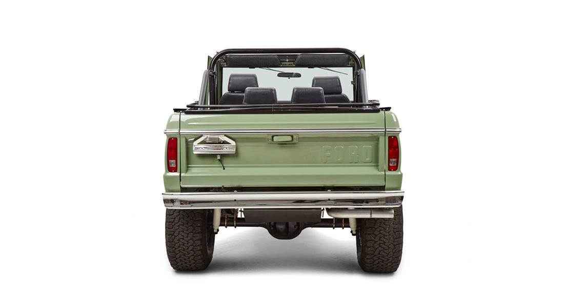 Back view of green Classic Ford Bronco with roll cage and open top, showing tailgate and tires.