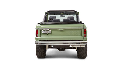 Back view of green Classic Ford Bronco with roll cage and open top, showing tailgate and tires.