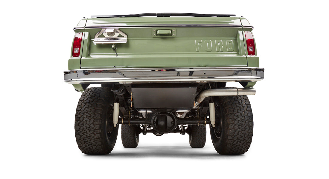 Rear view of lifted green Classic Ford Bronco showing large off-road tires and chrome bumper.