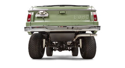 Rear view of lifted green Classic Ford Bronco showing large off-road tires and chrome bumper.