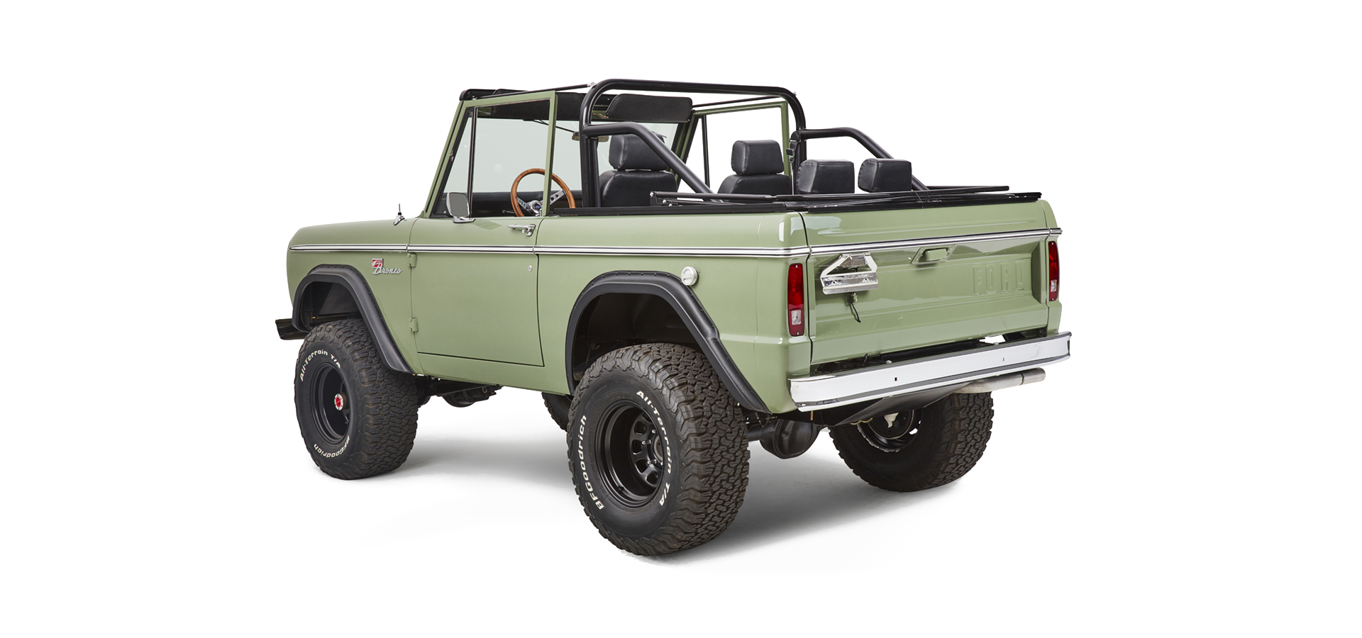Rear-side view of a green Classic Ford Bronco with black roll cage, steel wheels, and off-road tires