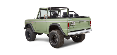 Rear-side view of a green Classic Ford Bronco with black roll cage, steel wheels, and off-road tires
