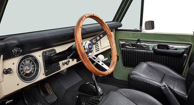 Interior of Classic Ford Bronco with wood steering wheel, dashboard, pedals, and black leather seats