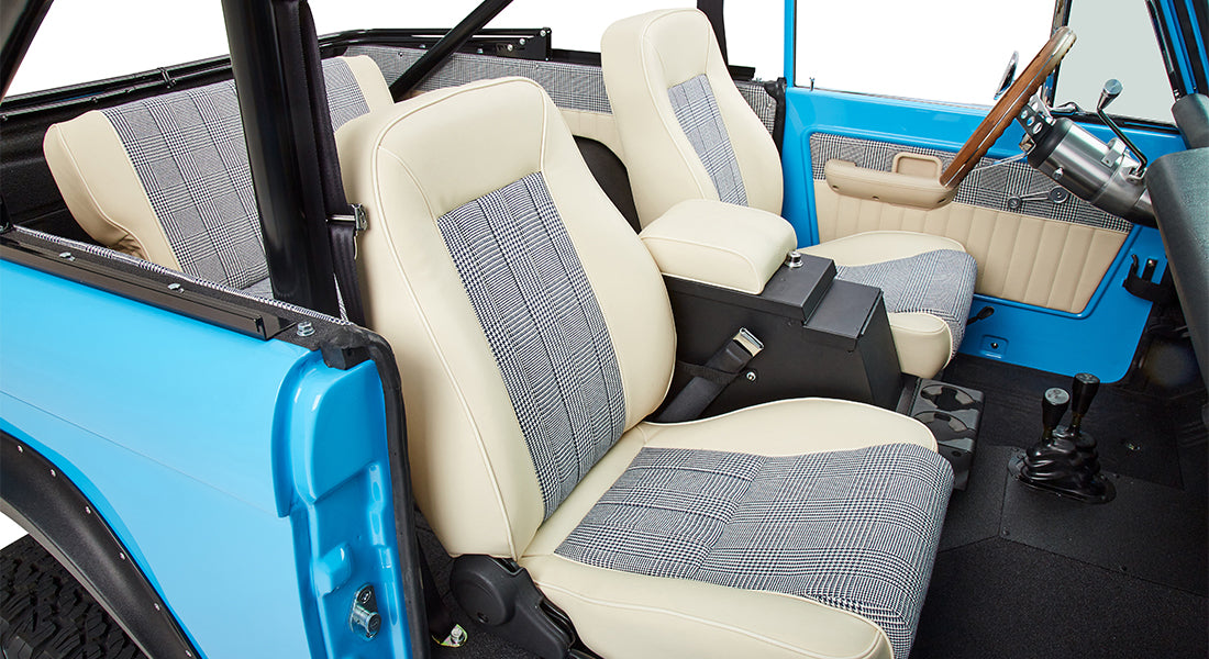 Interior cabin view of classic Ford Bronco with plaid fabric and cream seats, center console, and steering wheel