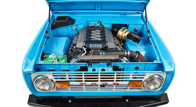 Front view of blue Classic Ford Bronco with hood open showing engine bay and grille